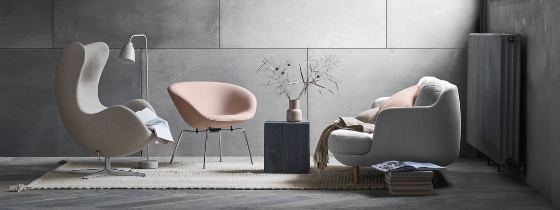 The Cosy Lune 2-seater sofa by Fritz Hansen with the matching Pot chair in soft grey and shades of pink. A modern living room ambiance in front of a grey wall.