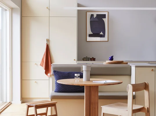 Angle stool, oak from Form & Refine in single view. The legs of the stool are connected by a band of naturally tanned leather attached to a brass rod.
