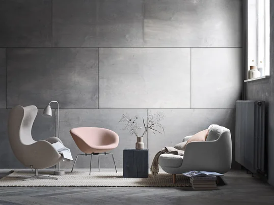 The Cosy Lune 2-seater sofa by Fritz Hansen with the matching Pot chair in soft grey and shades of pink. A modern living room ambiance in front of a grey wall.