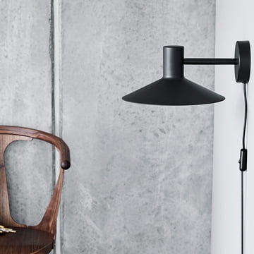 The Minneapolis wall light from Frandsen in black on a grey wall next to a dark wooden chair