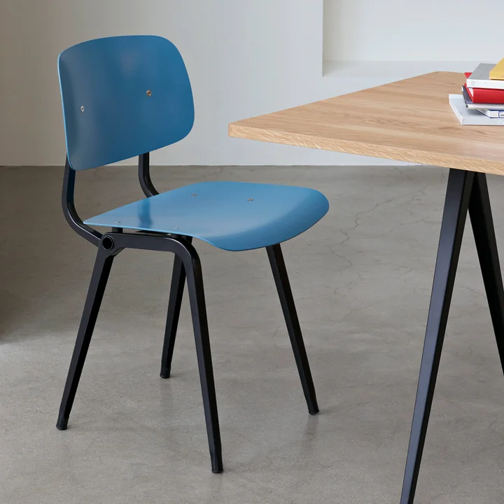 The Revolt Chair, black / azure blue by HAY on a wooden table with black legs