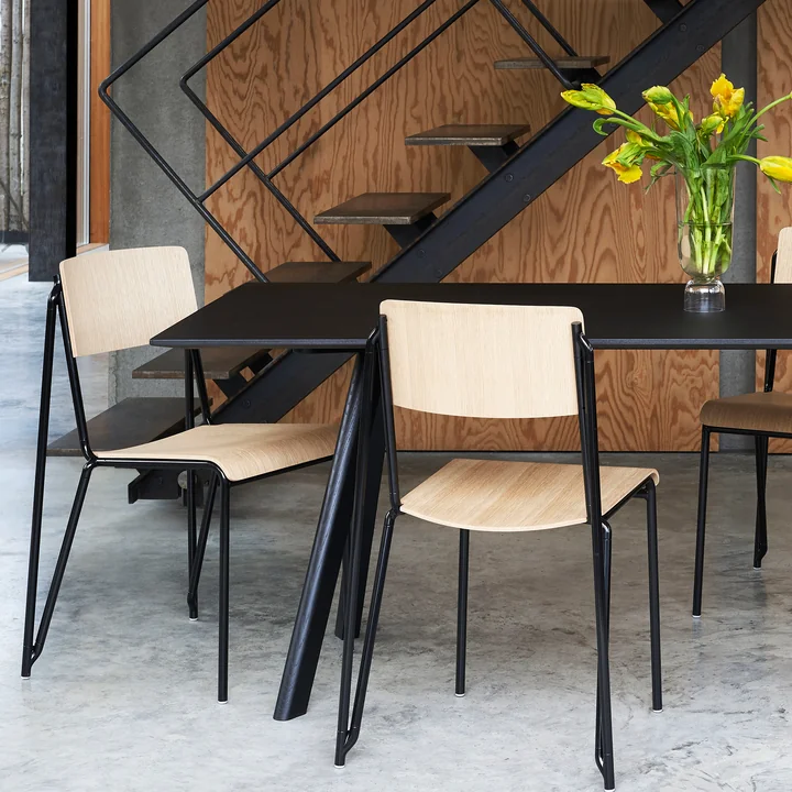 The Petit Standard chair, black / oak matt lacquered by HAY on a black table next to the stairs