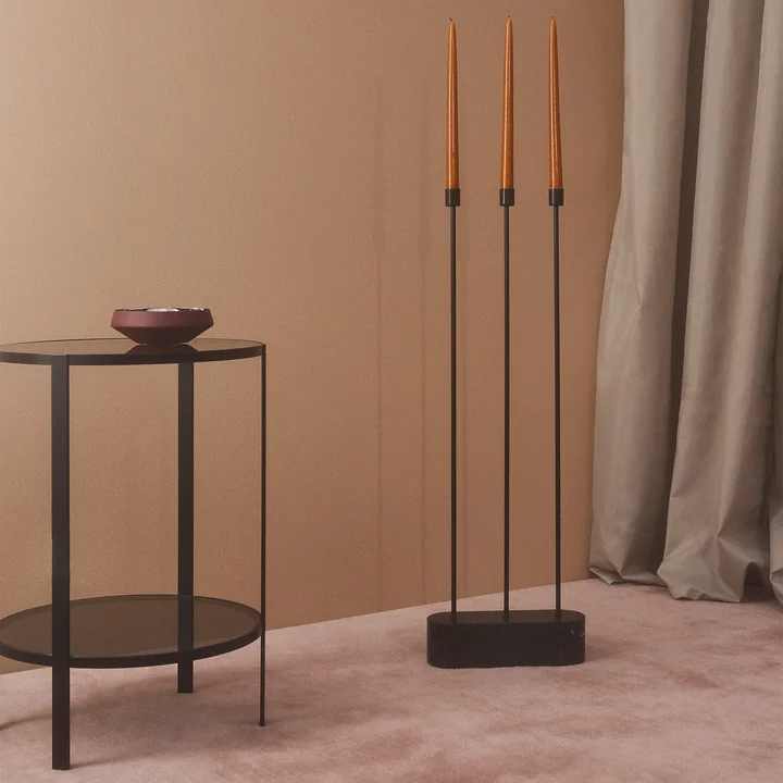 The Grasil candleholder for the floor next AYTM to a black side table in a room with lots of pink tones