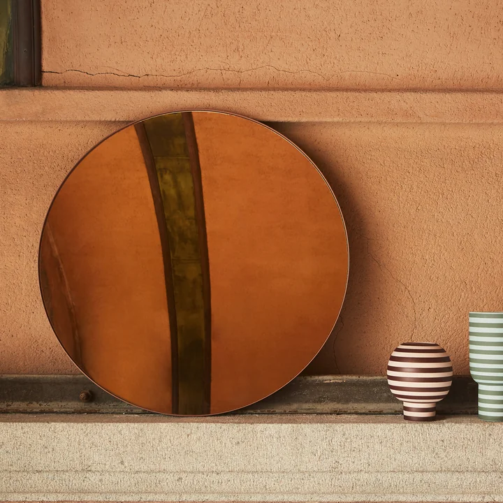 The Circum wall mirror with colored glass in the color amber from AYTM on a stone wall