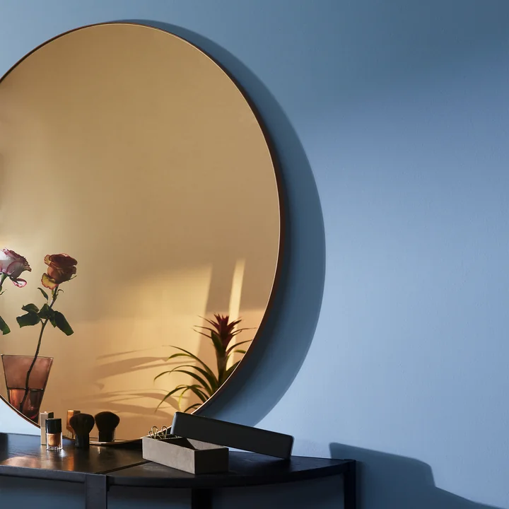 The Circum wall mirror from AYTM with colored glass in the color amber on a black sideboard