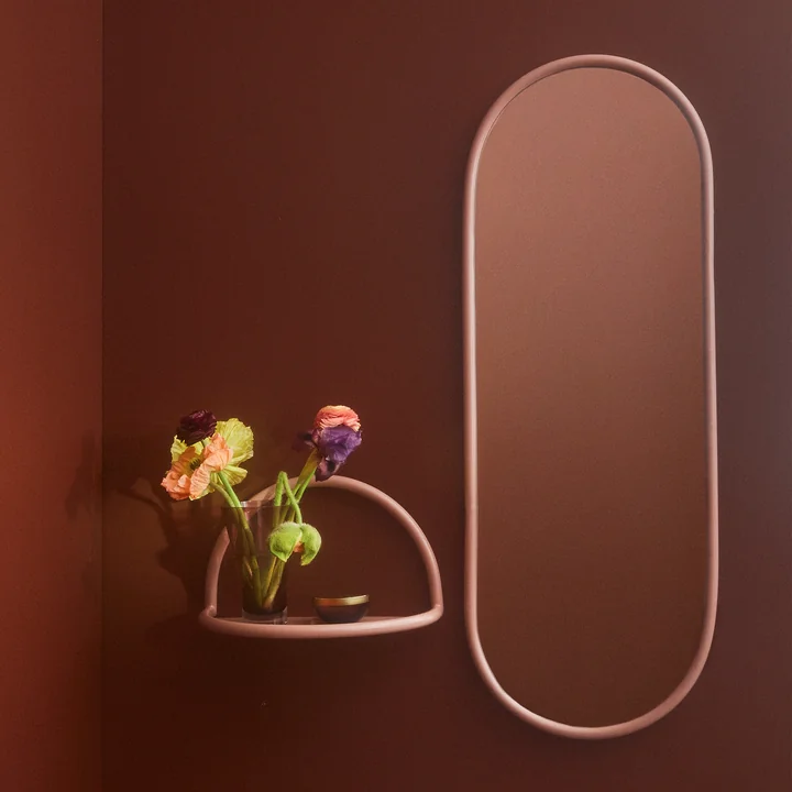 The Angui wall mirror with rose colored frame from AYTM next to a small wall shelf in the same color