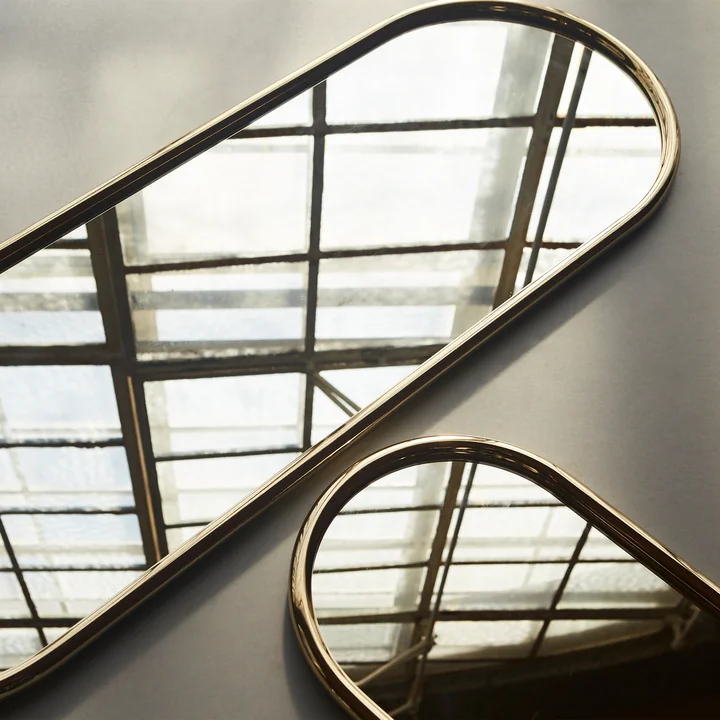 The Angui wall mirror from AYTM on the floor next to another wall mirror