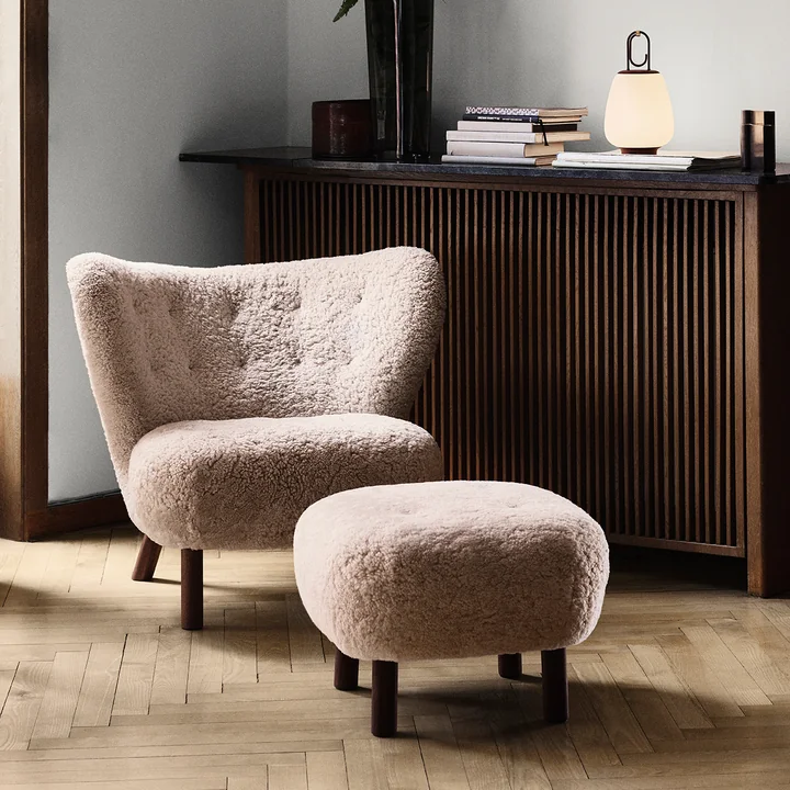 The Little Petra lounge chair with pouf from & Tradition in front of a dark radiator cladding