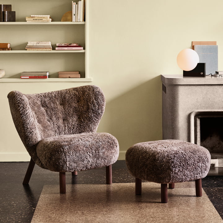 The Little Petra lounge chair with pouf from & Tradition in front of the stone fireplace in the living area