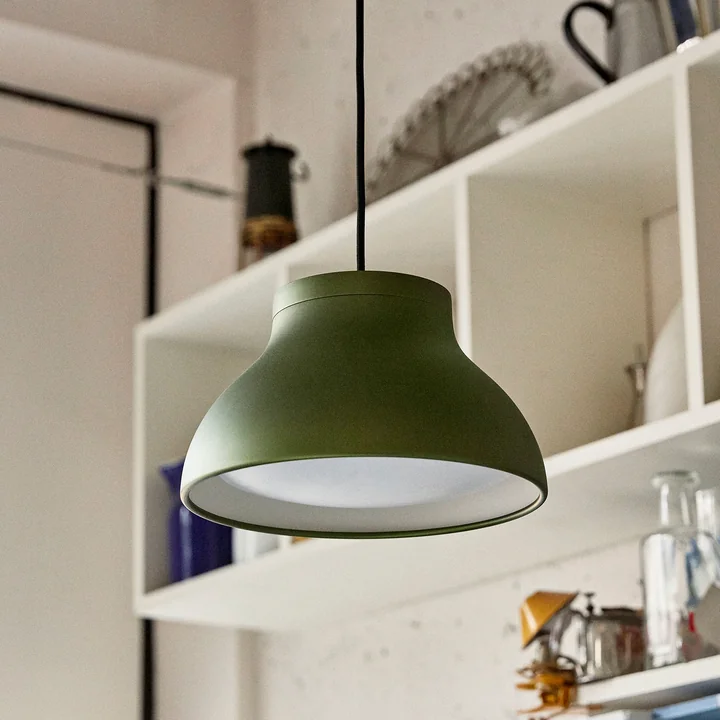 The PC pendant lamp from HAY in emerald green front of a wall shelf in the kitchen
