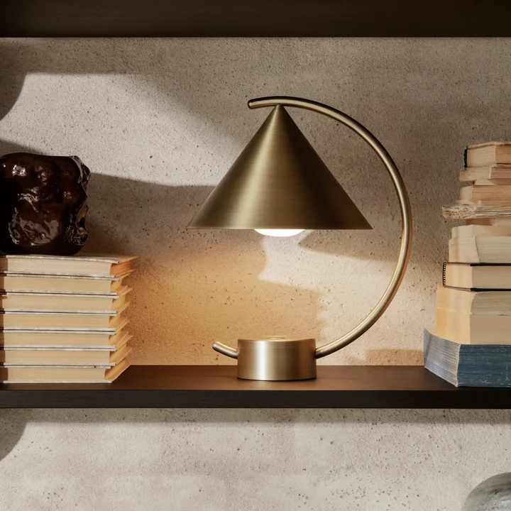 The Meridian table lamp by Ferm Living in brass on a shelf between books
