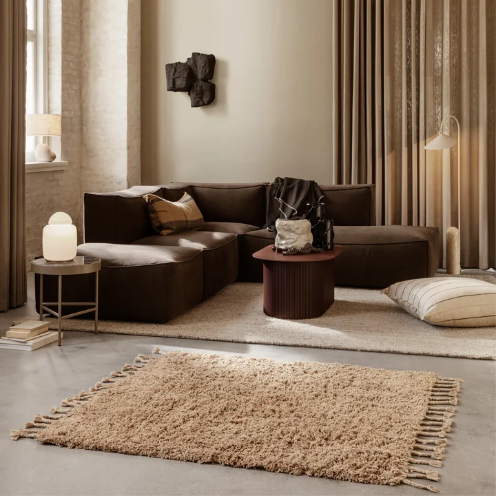 The Amass pile carpet by Ferm Living in an elegant living room with brown sofa and beige curtains.
