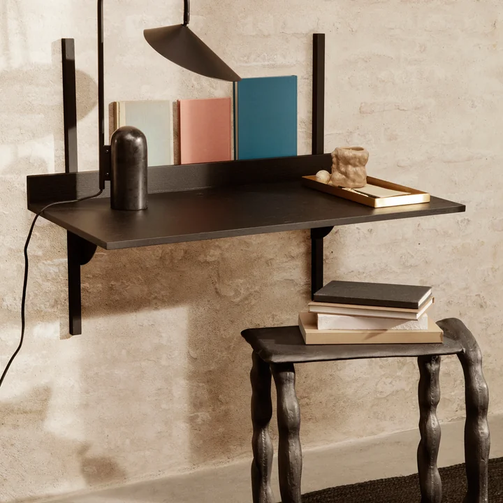 The Sector desk by Ferm Living on the wall in combination with books, a table lamp and a stool.