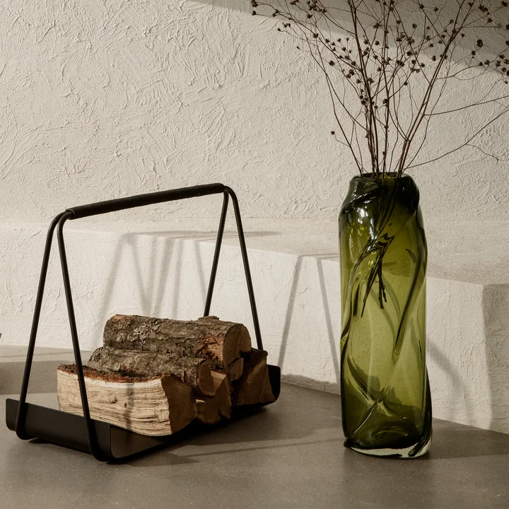 The Water Swirl vase by Ferm Living in moss green on the floor next to minimalist fireplace accessories.