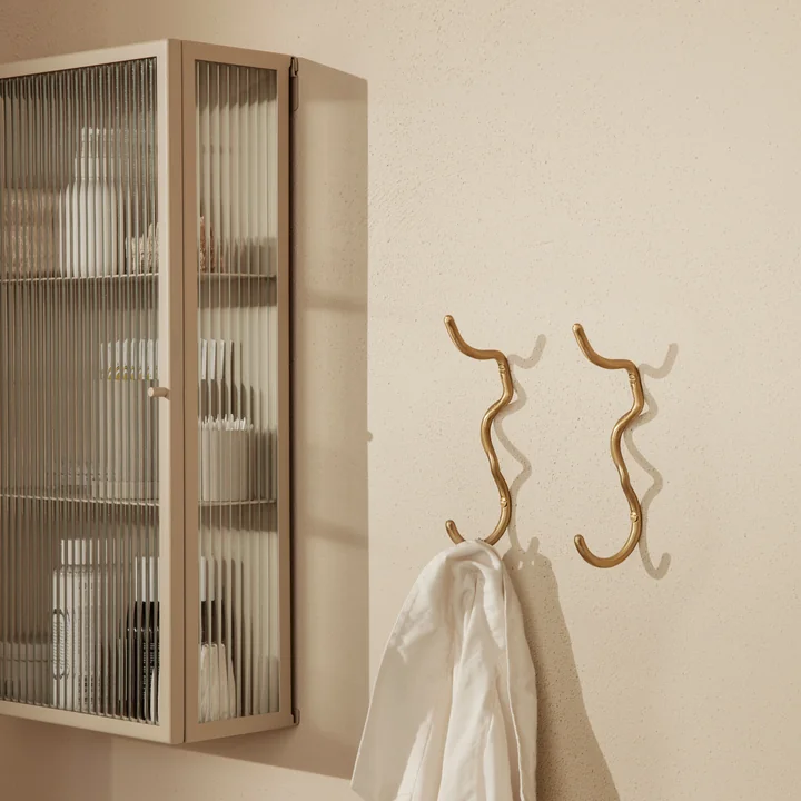 The Curvature wall hook by Ferm Living with a towel next to a wall display case