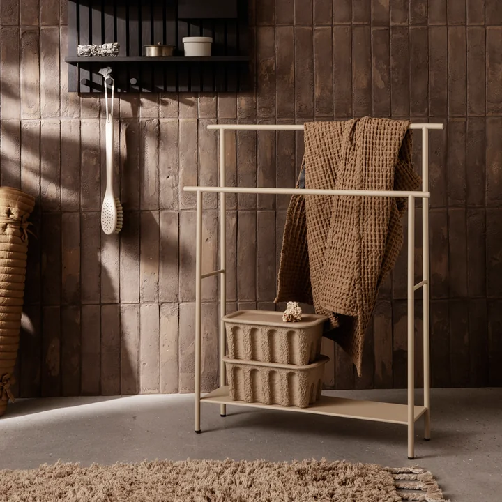 The Dora towel holder from Ferm Living with towels and paper boxes next to a wall shelf
