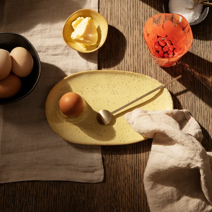 The yellow Flow breakfast plate by Ferm Living next to glasses on a beige tablecloth