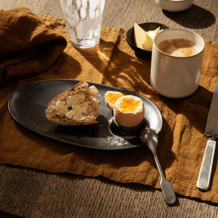 The Flow breakfast plate by Ferm Living with bread and egg on a brown tablecloth