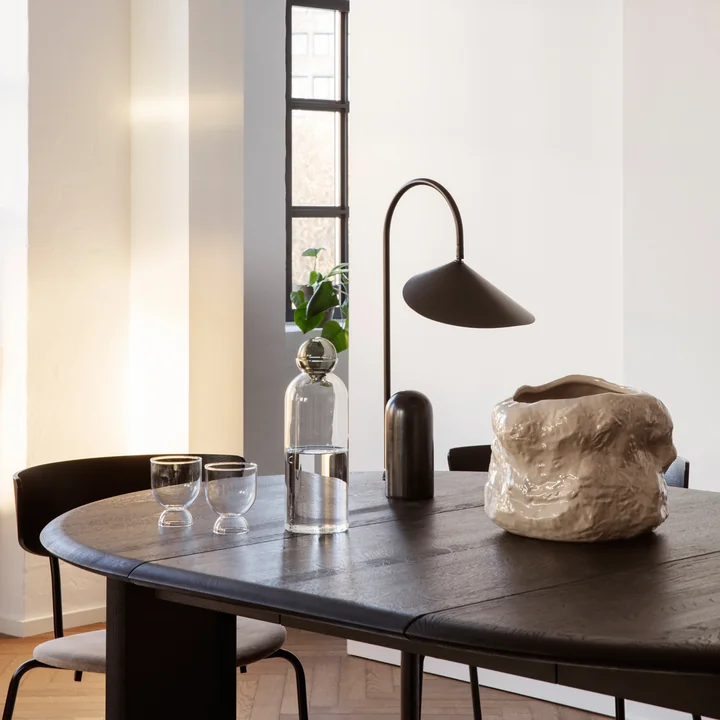 The Tuck plant pot from Ferm Living on a dark wooden dining table next to a black table lamp