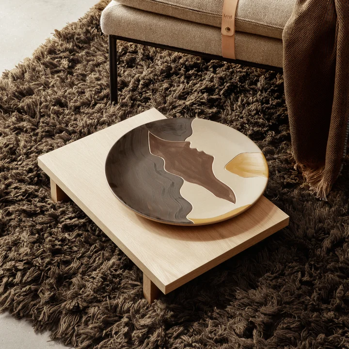 The Kona Low side table from Ferm Living on a cozy, brown rug next to a daybed