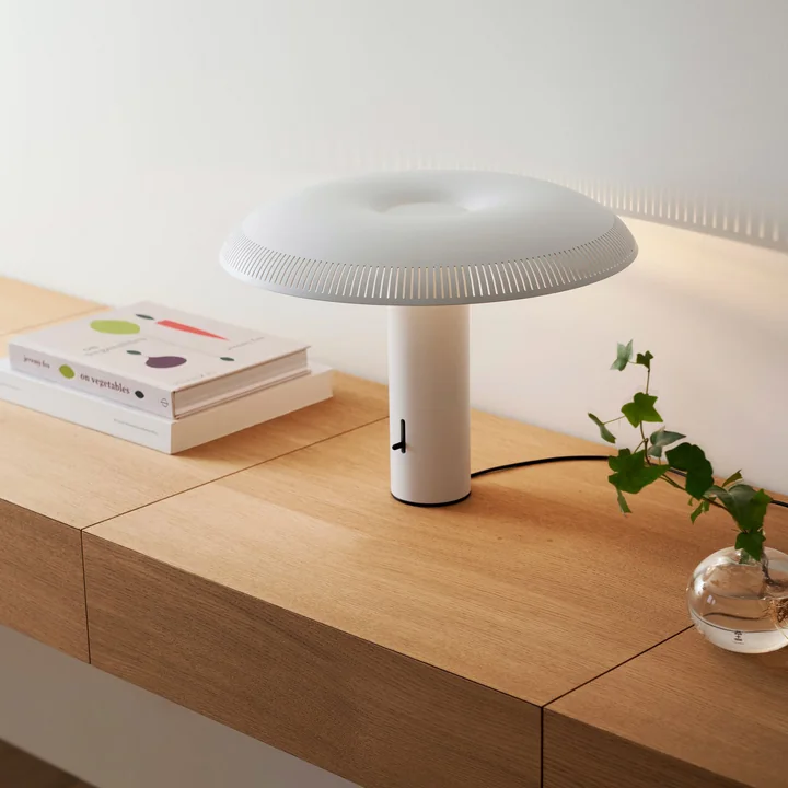 The w203 Ilumina LED table lamp by Wästberg in white on a wooden bench next to books and vases