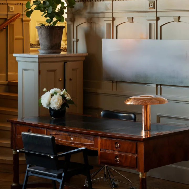 The w203 Ilumina LED table lamp from Wästberg in copper on an antique desk in a noble ambience with a lot of wood.