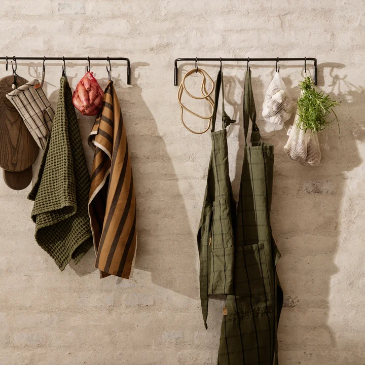 The Organic towel from Ferm Living alongside other towels and kitchen aprons on a hook rail
