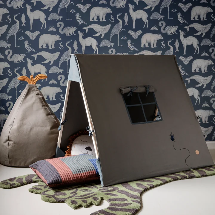 The play tent of Ferm Living in olive on a tiger carpet in front of a blue wallpaper