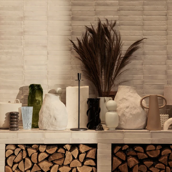 The Vulca Vase by Ferm Living next to other vases and art objects on a stone bench