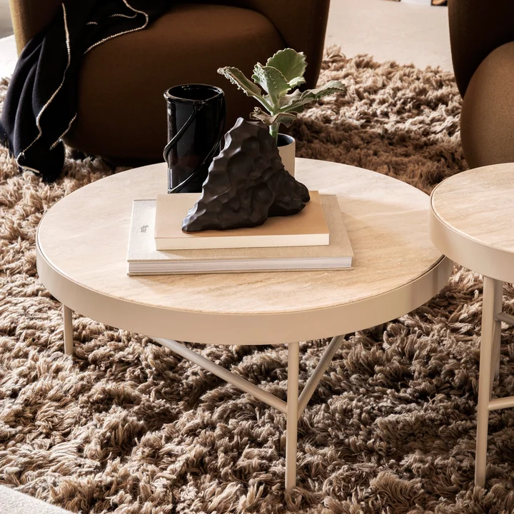 The large Travertine coffee table by Ferm Living with books and art objects on a fluffy carpet