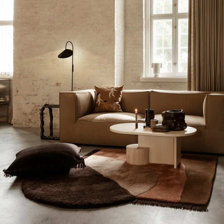 The Kelim Cushion by Ferm Living on a large carpet with patchwork pattern in the living room with many earthy tones