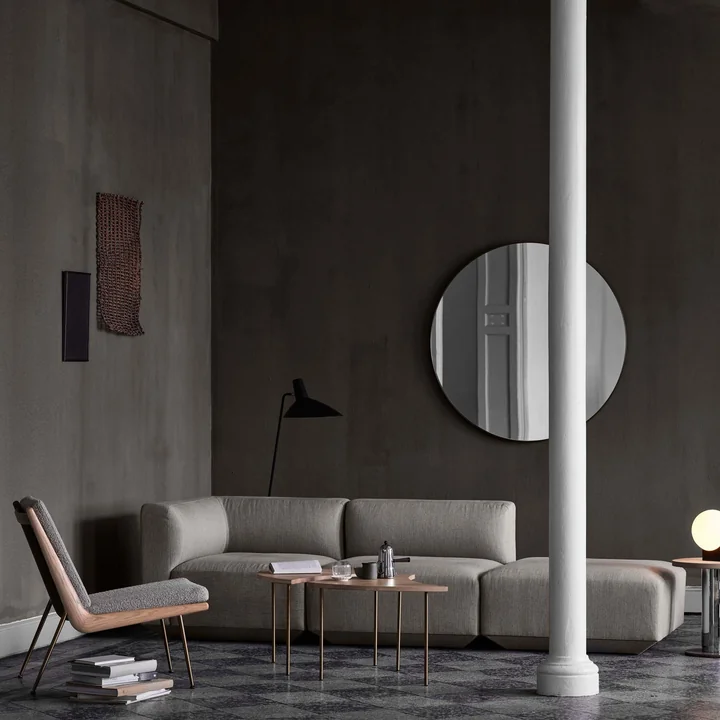 The Amore mirror around by & tradition in a large, dark living area over a grey sofa