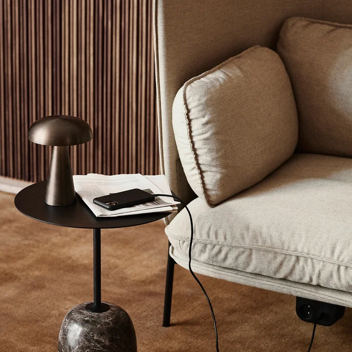 The Como SC53 rechargeable lamp from & Tradition on a black side table next to a light-colored couch