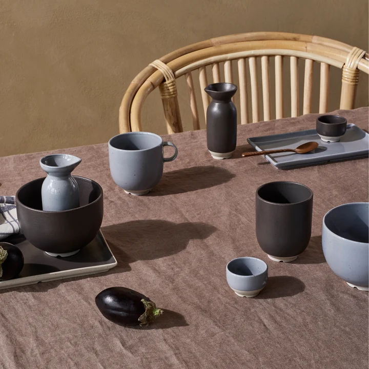 The Eli tableware from Broste Copenhagen in soft blue and charoal on the dining table next to a rattan chair