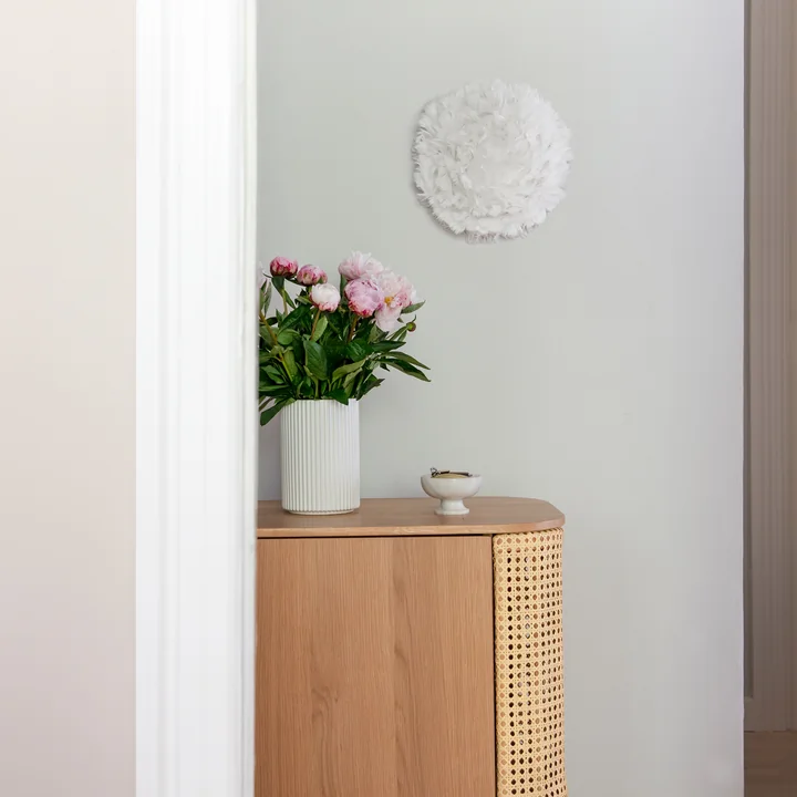 The EOS Up ceiling and wall lamp Mini from Umage in créme over a wooden sideboard and flowers