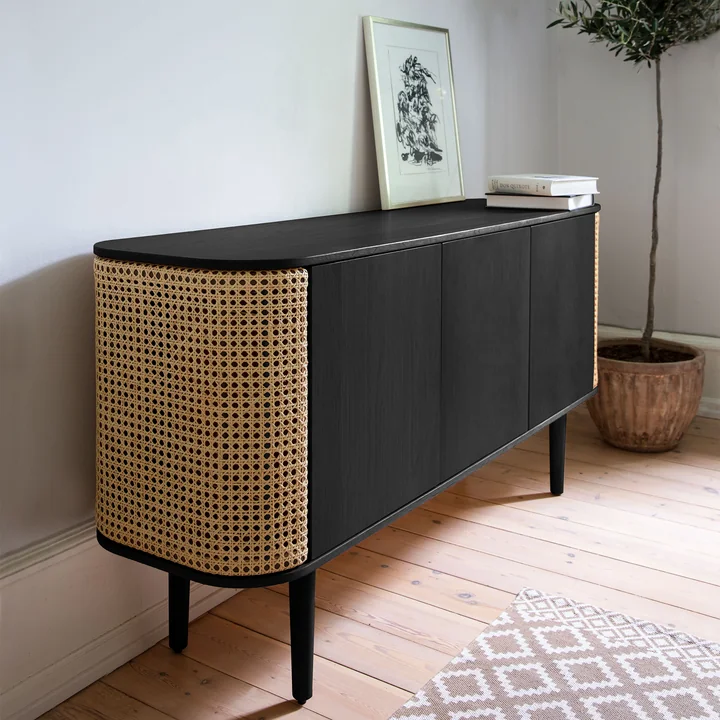 The Treasures Sideboard of Umage in black / Viennese wickerwork next to a houseplant and pictures