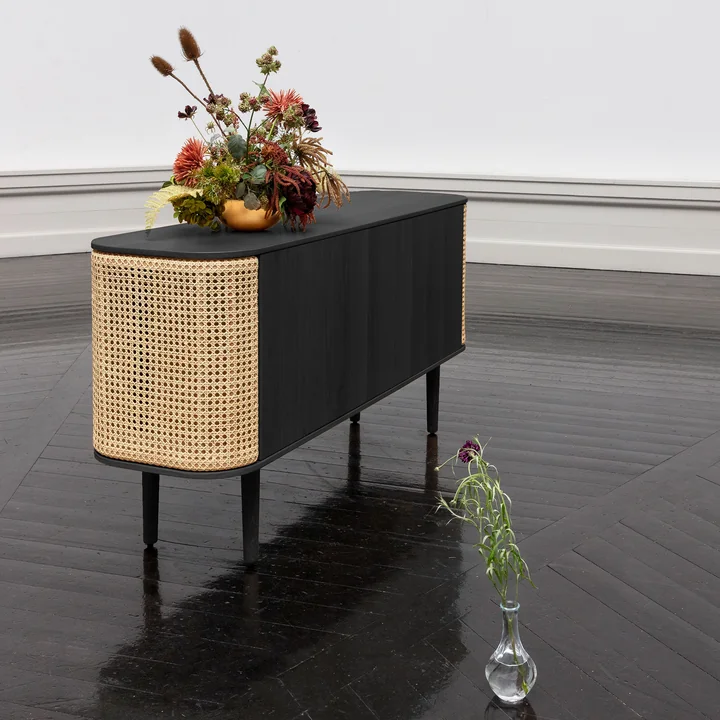 The Treasures Sideboard of Umage in black / Viennese wicker with flowers on a black parquet floor