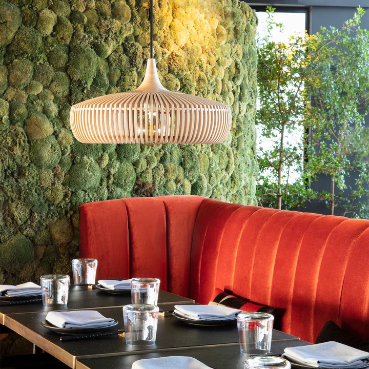 The Clava Dine Wood lampshade from Umage in oak above the tables in a restaurant with red sofas