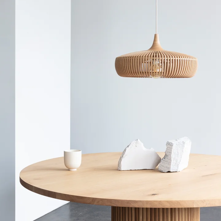 The Clava Dine Wood lampshade from Umage in oak above a bright, round wooden table
