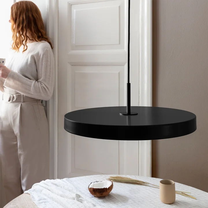 The Asteria LED pendant light from Umage in black / black above a round, white dining table