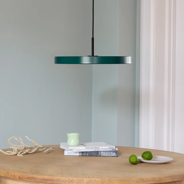 The Asteria LED pendant light from Umage in black / forest green above a bright, round wooden dining table