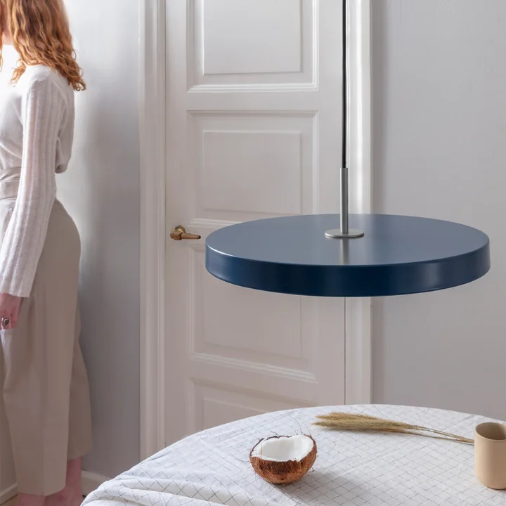 The Asteria LED pendant light from Umage in steel / petrol above a round dining table with a checkered ceiling