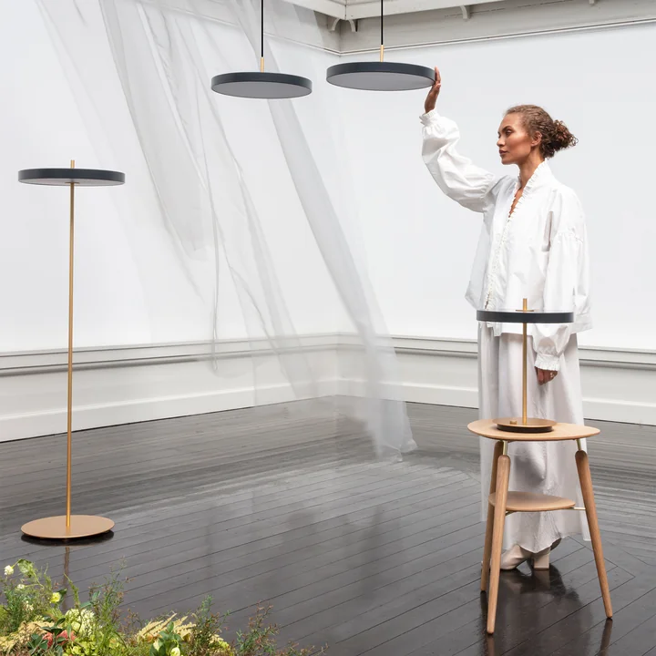 The Asteria Luminaires from Umage in brass / black in a large room with veils and plants