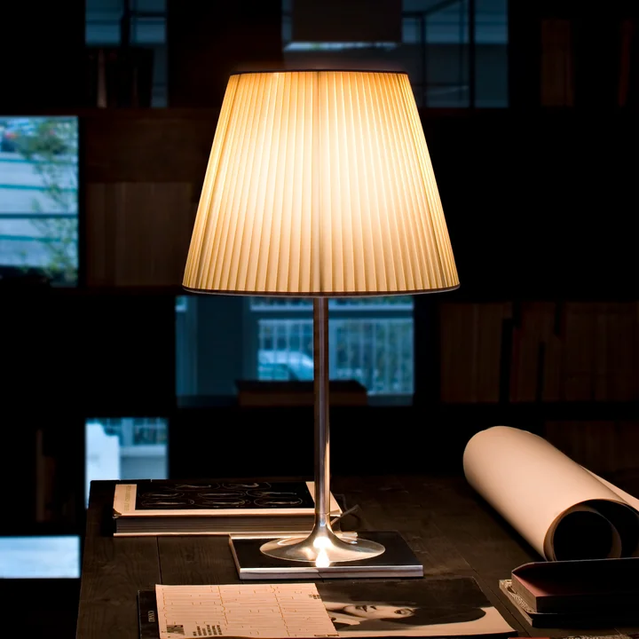 The luminous K Tribe T2 table lamp from Flos with fabric shade beside magazines and posters