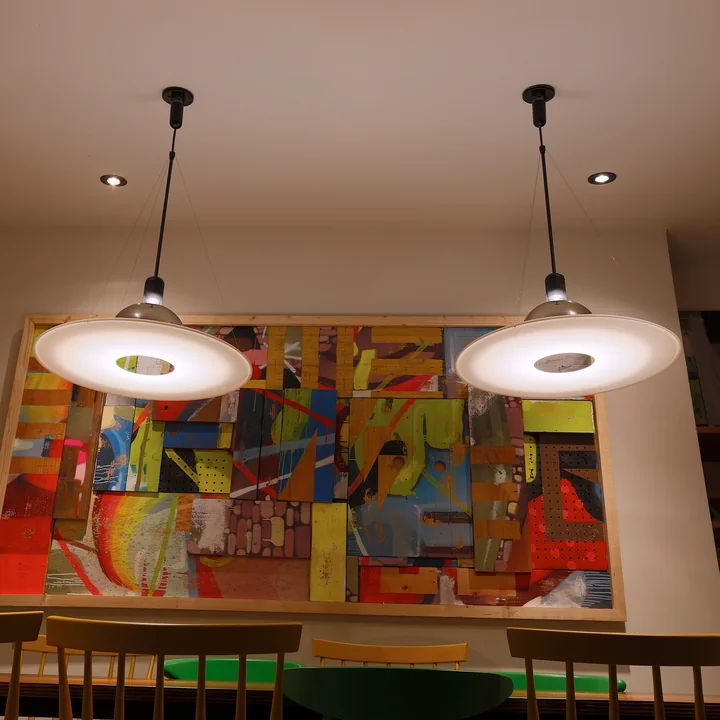 The Frisbi pendant lamp from Flos above a dining table in front of a colourful work of art