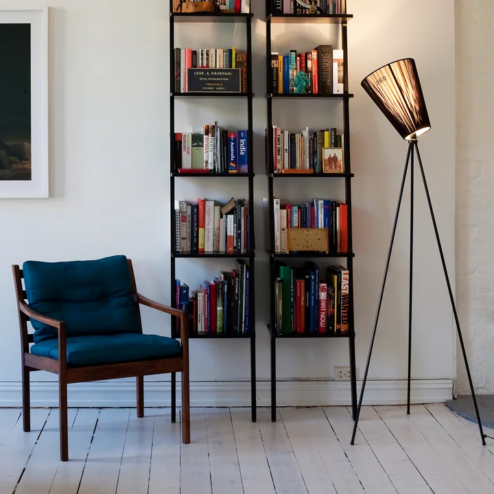 The Oslo Wood floor lamp from Northern next to bookshelves and a petrol blue armchair