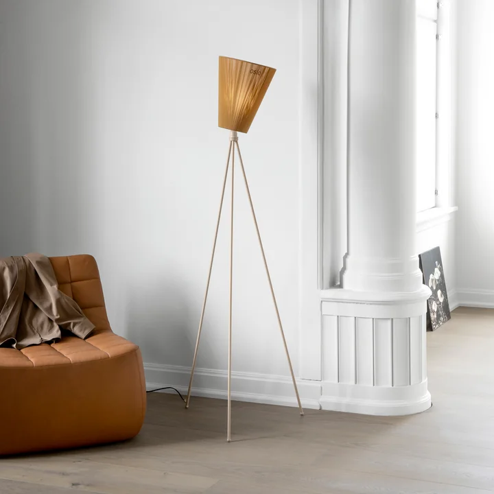 The Oslo Wood floor lamp from Northern beside a brown leather armchair and a white wall