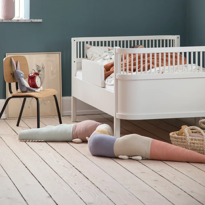 The playful Sleepy Croc pillow from Sebra next to the white crib