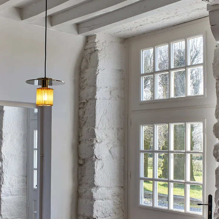 The In the Sun pendant luminaire by DCW in a room with white stone walls and wooden beams