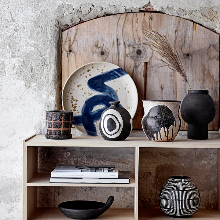 The Oscar wall plate from Bloomingville on a wooden sideboard next to vases and decorative objects.